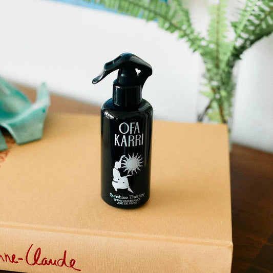 Schwarze Ofa Karri Raumduftspray-Flasche auf Buch, im Hintergrund Pflanzen
