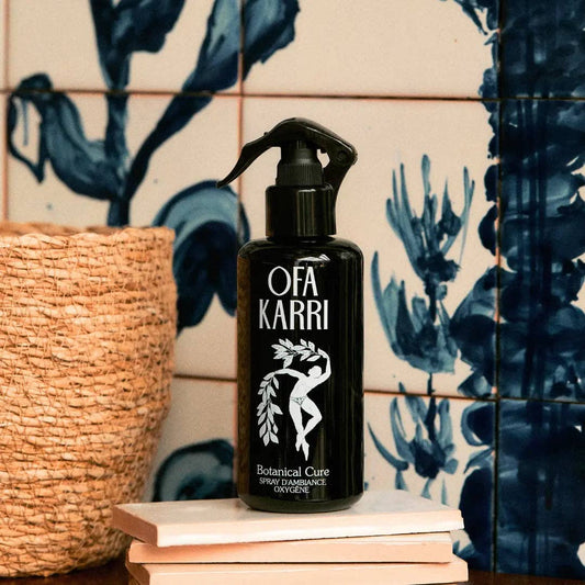 Schwarze Sprayflasche Ofa Karri Botanical Cure auf weißen Fliesen mit blauem Muster, neben geflochtenem Korb.
