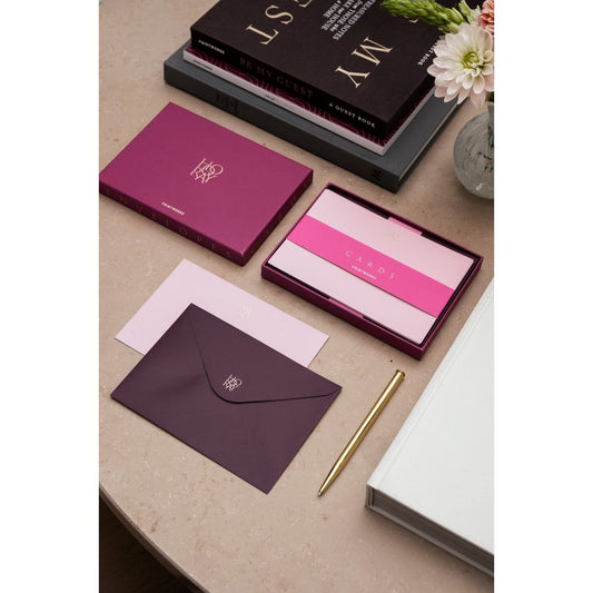 Elegantes Briefpapier-Set in Lila und Rosa mit Umschlägen, Karten und goldenem Stift auf Tisch