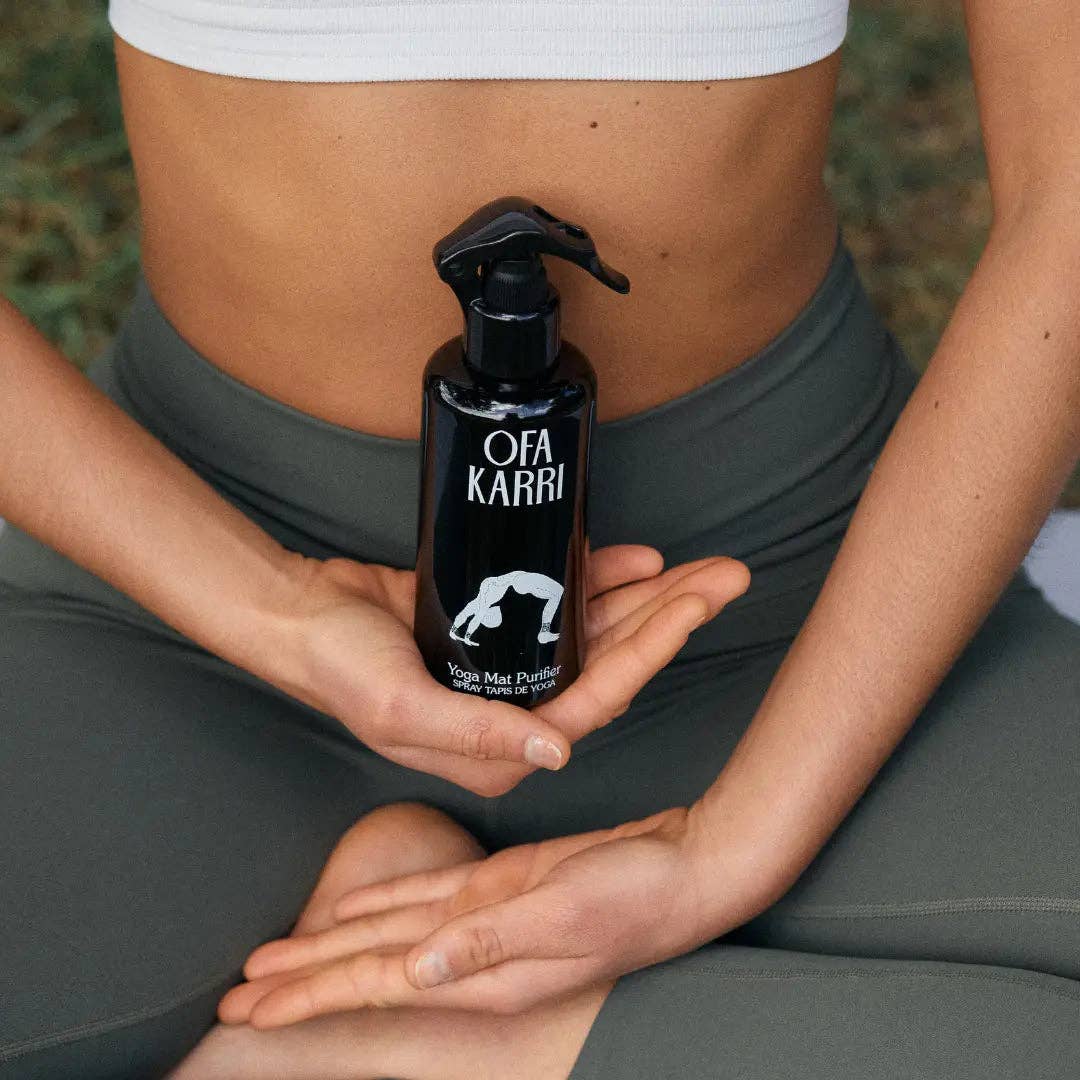 Frau in Sportkleidung hält Yoga Matten Reiniger Ofa Karri, sitzt im Meditationssitz draußen