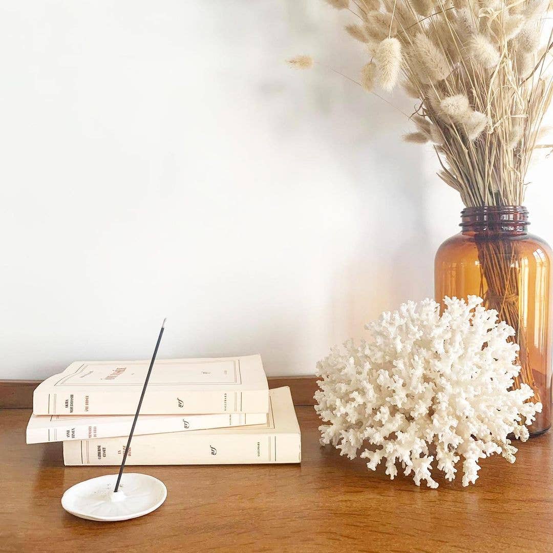 Minimalistische Deko mit Räucherstäbchenhalter, Büchern, Koralle und Vase mit Trockenblumen auf Holzkommode