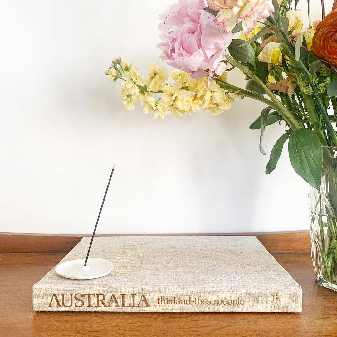 Raumdeko mit Blumenstrauß in Vase, Buch und Keramik Räucherstäbchenhalter auf Holzfläche