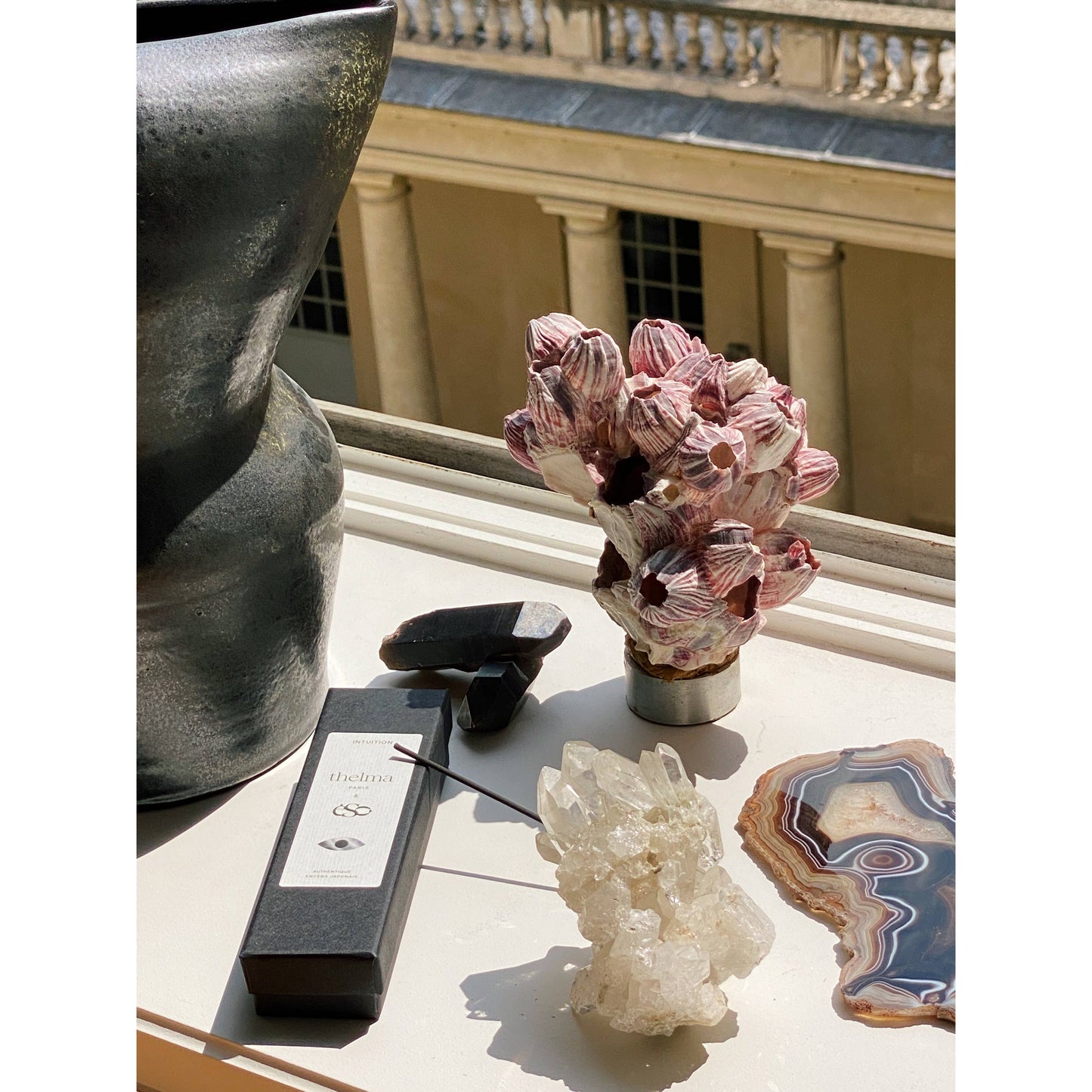 Fensterbank mit dekorativen Kristallen, Räucherstäbchen und Keramikvase in Sonnenlicht