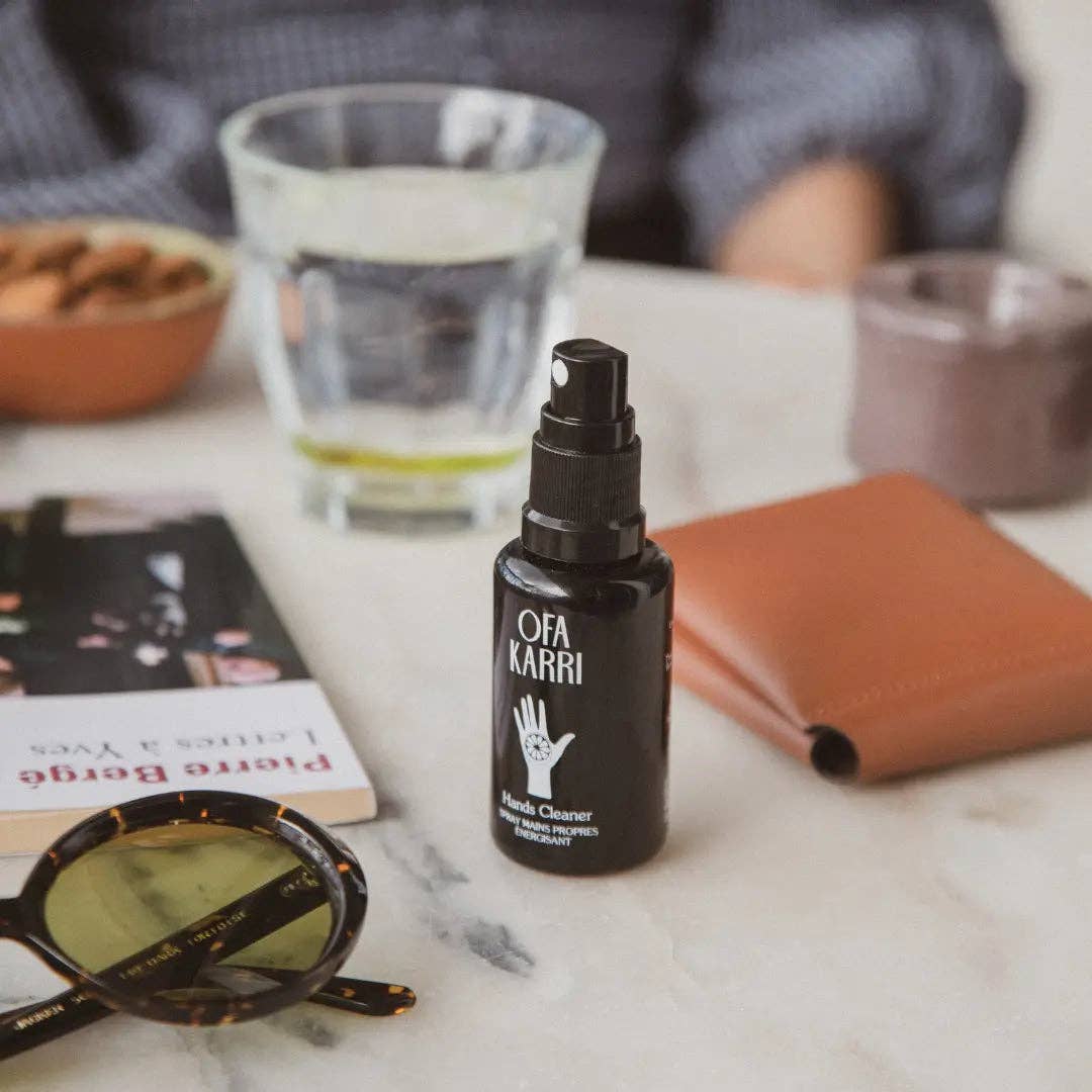 Handreiniger Spray Ofa Karri auf Tisch mit Sonnenbrille, Buch, Glas Wasser und Portemonnaie