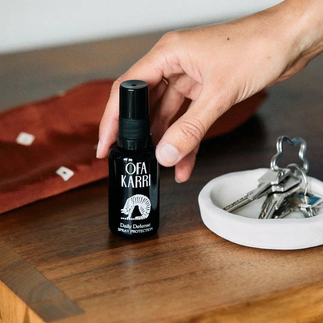 Hand greift zu OFA KARRI Daily Defense Spray auf Holztisch neben Schlüssel und Schale