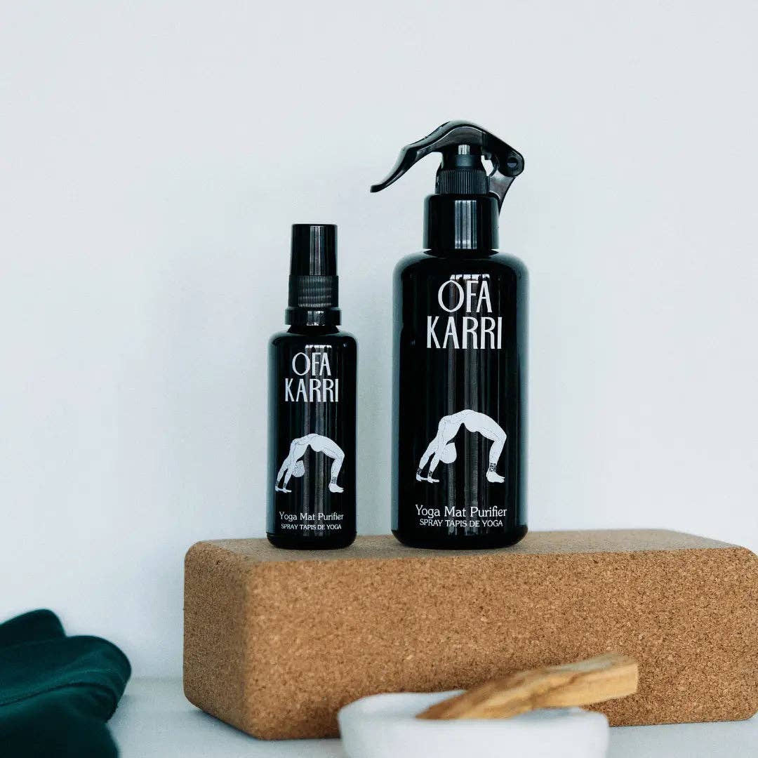Zwei schwarze Yoga Mattenreiniger Sprays auf Korkblock, umgeben von Yoga-Zubehör.