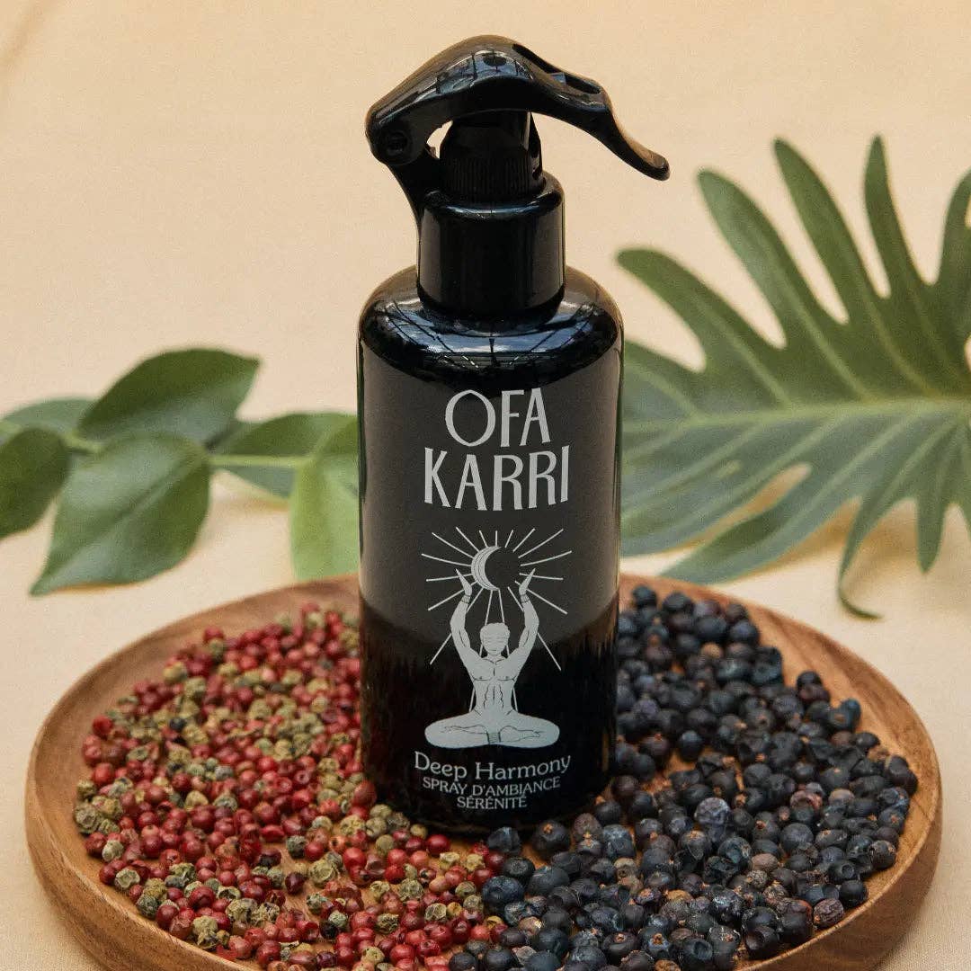 Schwarze Ofa Karri Deep Harmony Raumduftspray-Flasche auf Holzteller mit Pfefferkörnern und Blättern