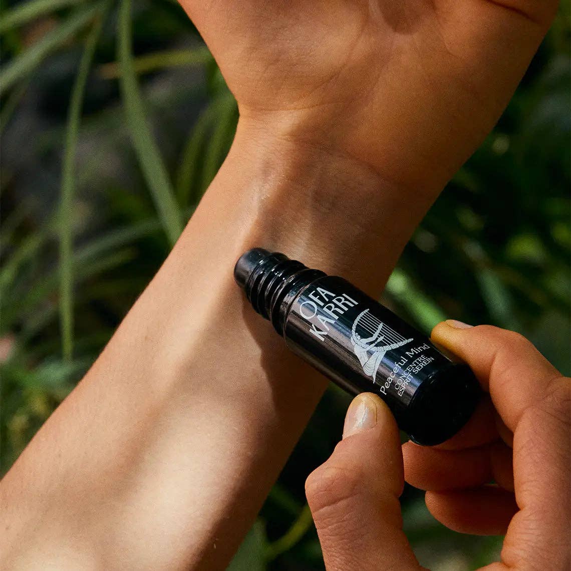 Aromatherapie Roll-On mit ätherischen Ölen wird auf das Handgelenk aufgetragen, Natur im Hintergrund