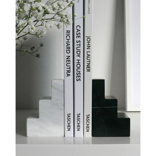 Stufenförmige Buchstützen aus Marmor in Weiß und Schwarz halten Bücher auf einem Regal.