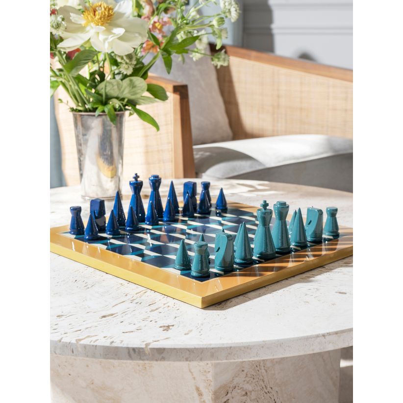 Modernes Schachspiel mit blauen Figuren auf Marmortisch, Blumen und Sofa im Hintergrund