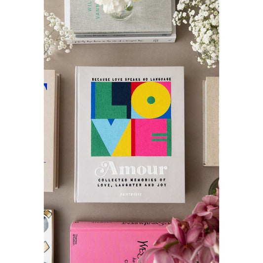 Buch mit bunter LOVE-Aufschrift auf einem Tisch, umgeben von Blumen und weiteren Büchern, Deko, Lifestyle