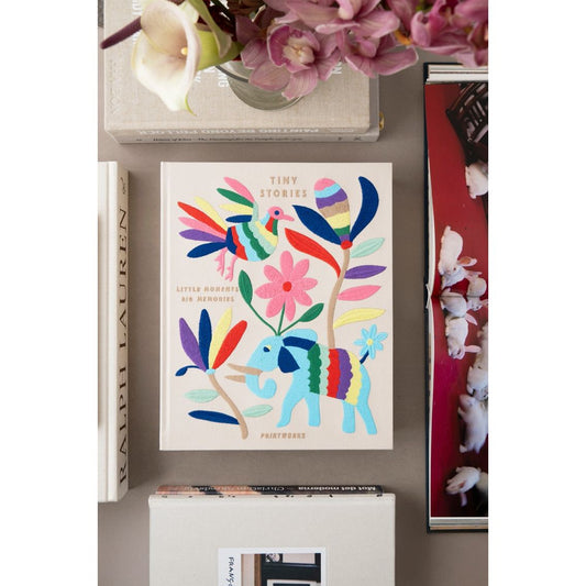 Fotoalbum mit buntem Tier- und Blumenmotiv auf Tisch zwischen Blumen und Fotobüchern
