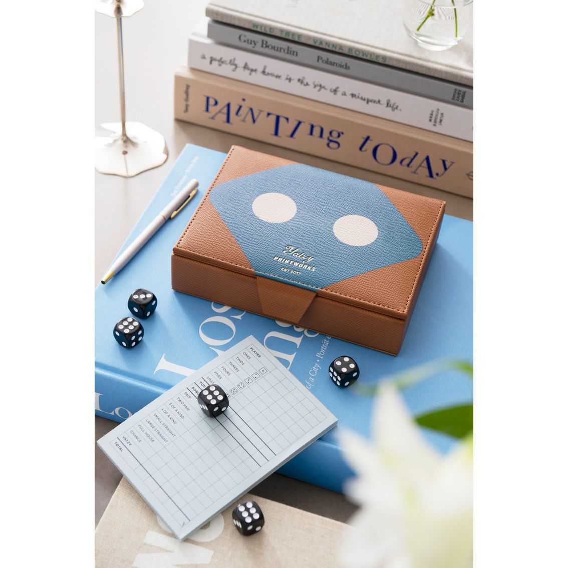 Stylisches Würfelspiel-Set aus Leder auf Tisch mit Spielblock, Würfeln und Büchern, für analoge Spieleabende.