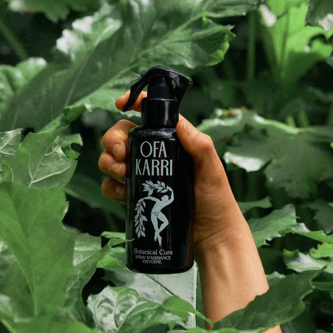 Hand hält schwarze Flasche Ofa Karri Botanical Cure Spray vor grünen Blättern, Naturprodukt