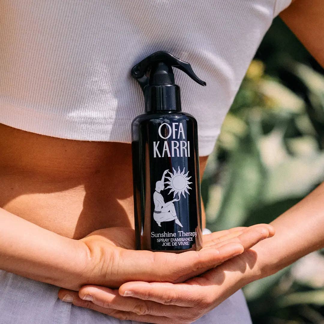 Schwarze Flasche Ofa Karri Sunshine Therapy Spray, gehalten vor weißem Top, Naturhintergrund
