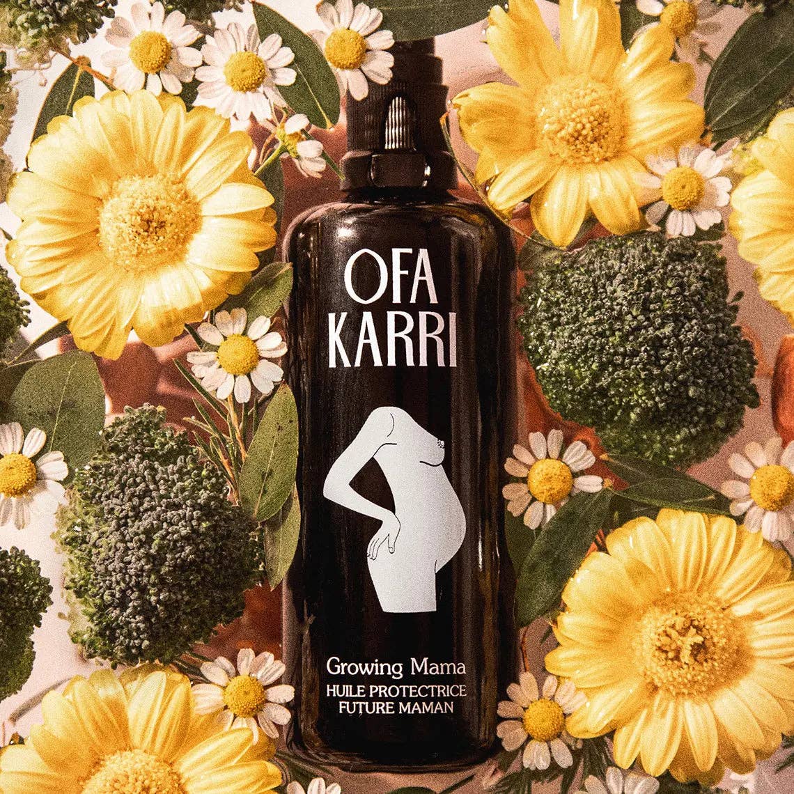 Schwarze Flasche Ofa Karri Hautöl für Schwangere, umgeben von gelben Blumen und Brokkoli