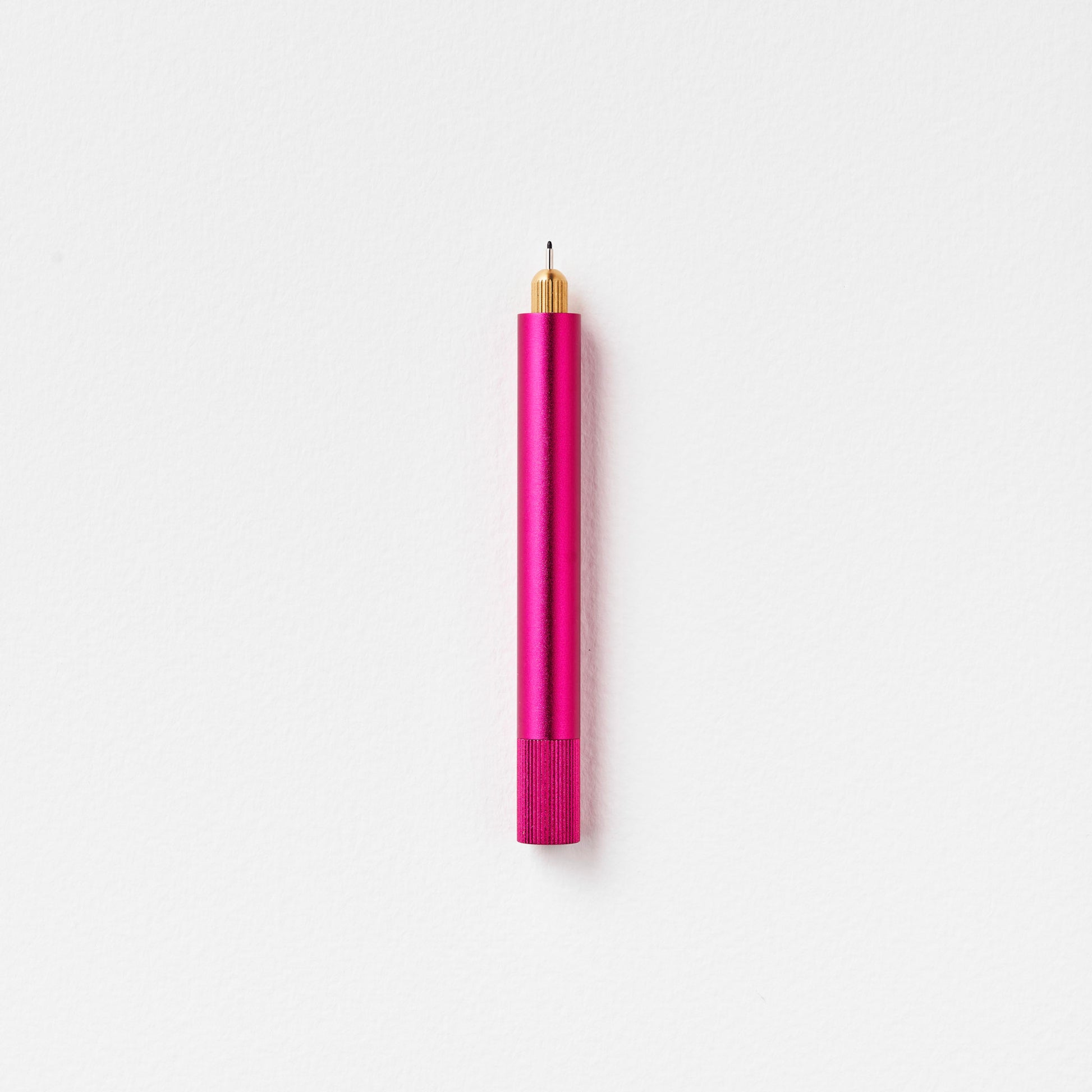 Minimalistischer Stift aus Metall in Pink mit goldener Spitze auf weißem Hintergrund