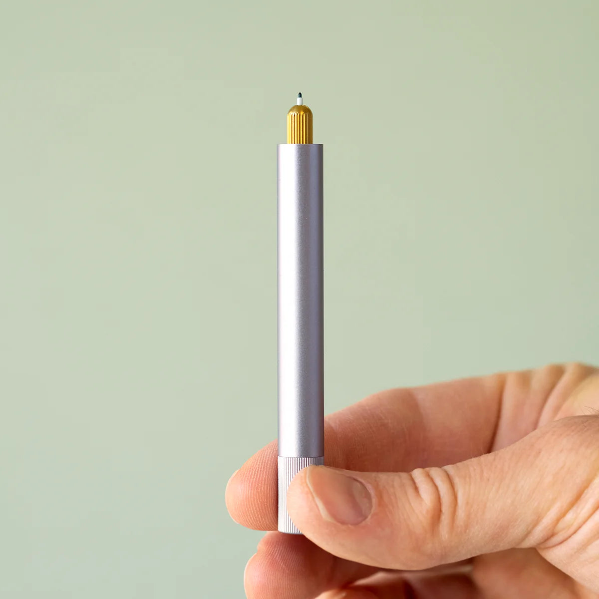 Minimalistischer silberner Stift mit goldener Spitze, gehalten von einer Hand vor hellem Hintergrund